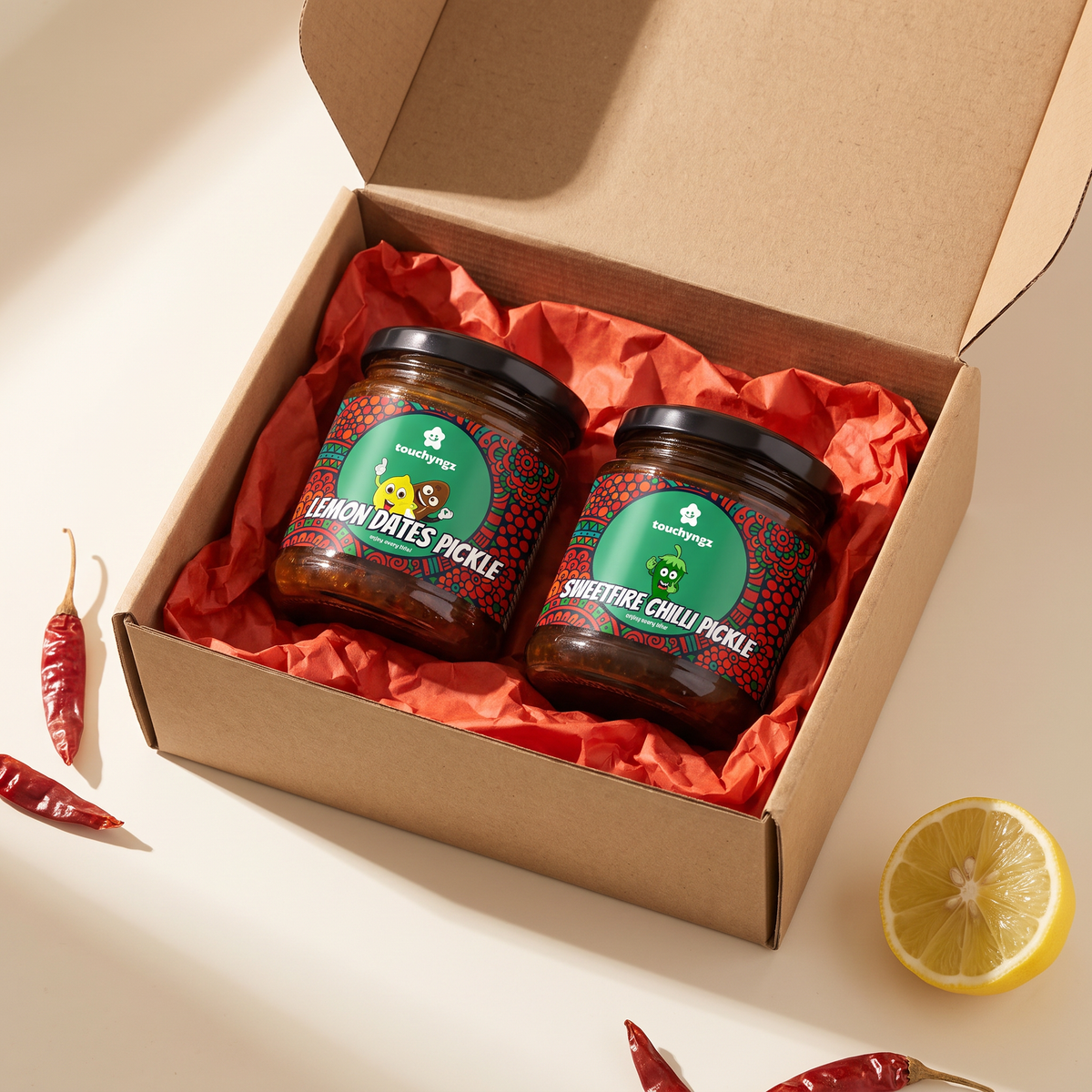 Kerala Veg Pickle Gift Box by Touchyngz — Lemon Dates Pickle and SweetFire Chilli Pickle jars in an open kraft gift box with red tissue paper
